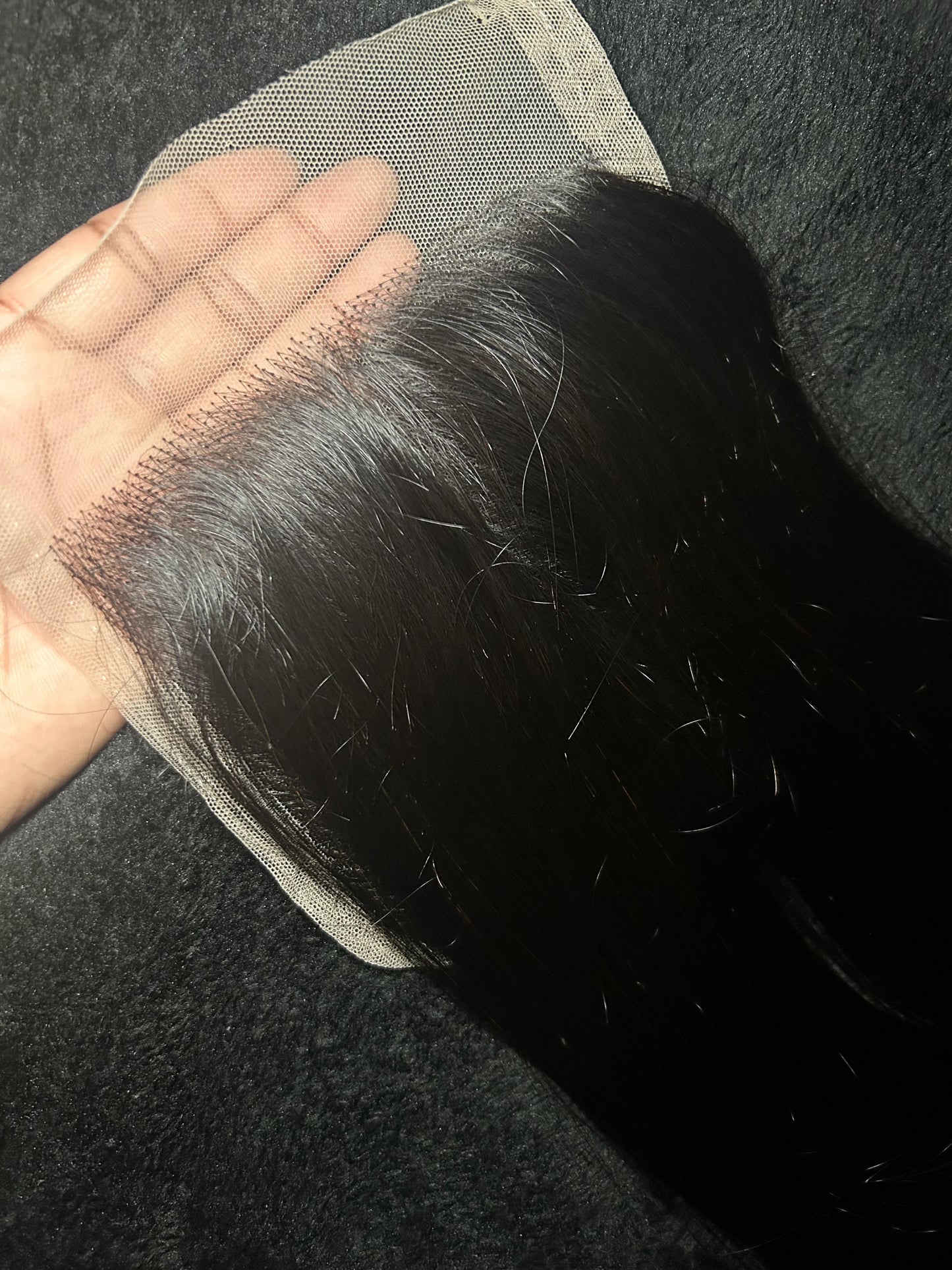 Hand holding straight black lace closure hair extension on dark textured background