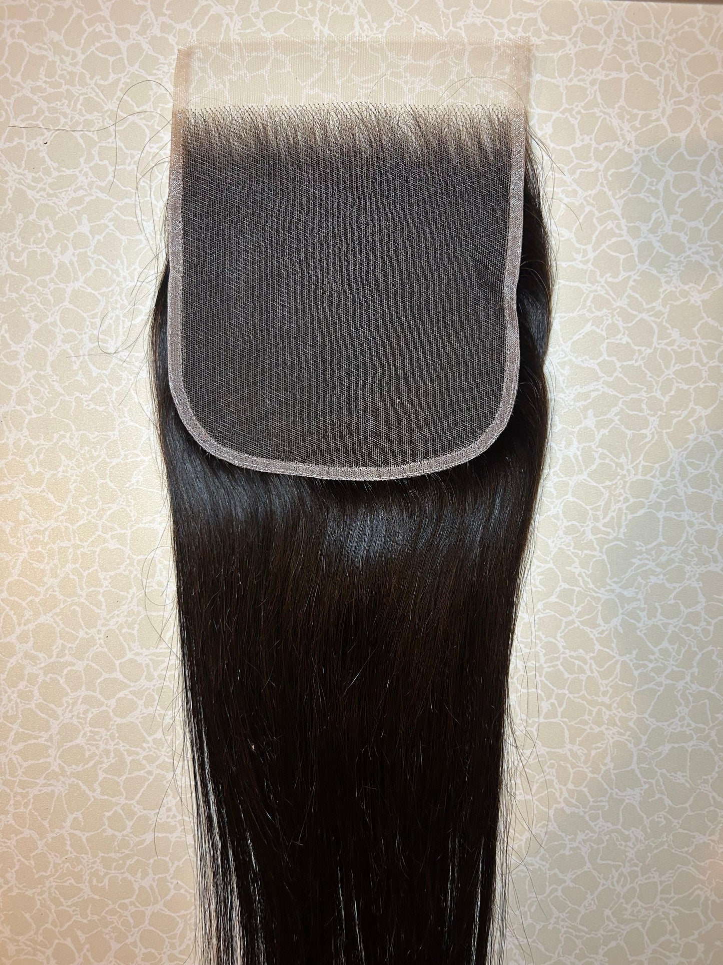 Straight black lace hair closure with natural shine on patterned background