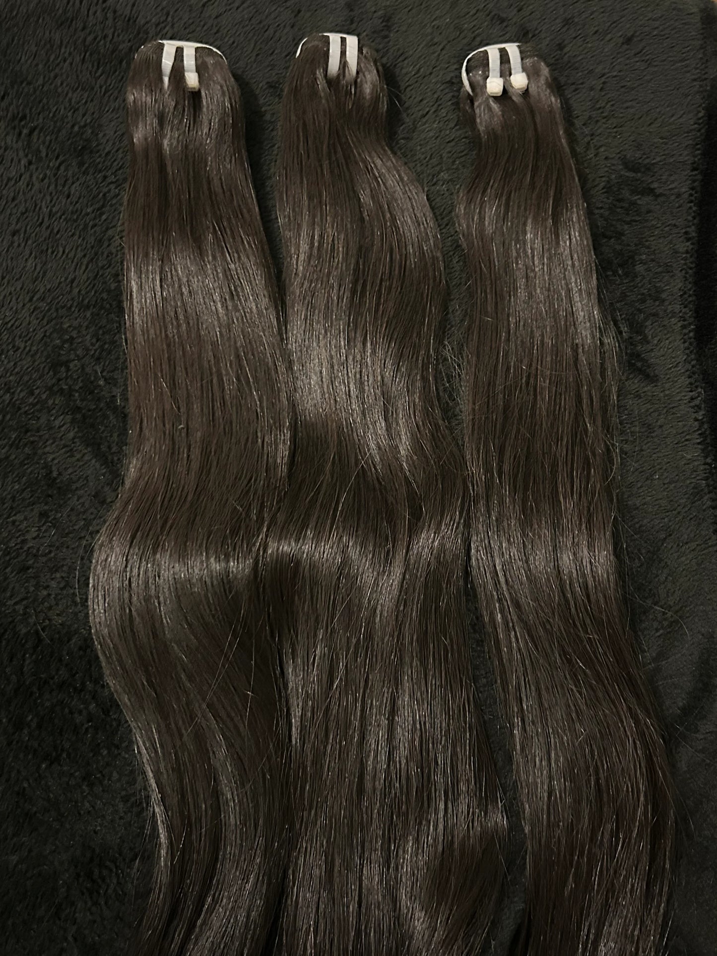 Three bundles of raw black straight hair extensions on a black fabric background