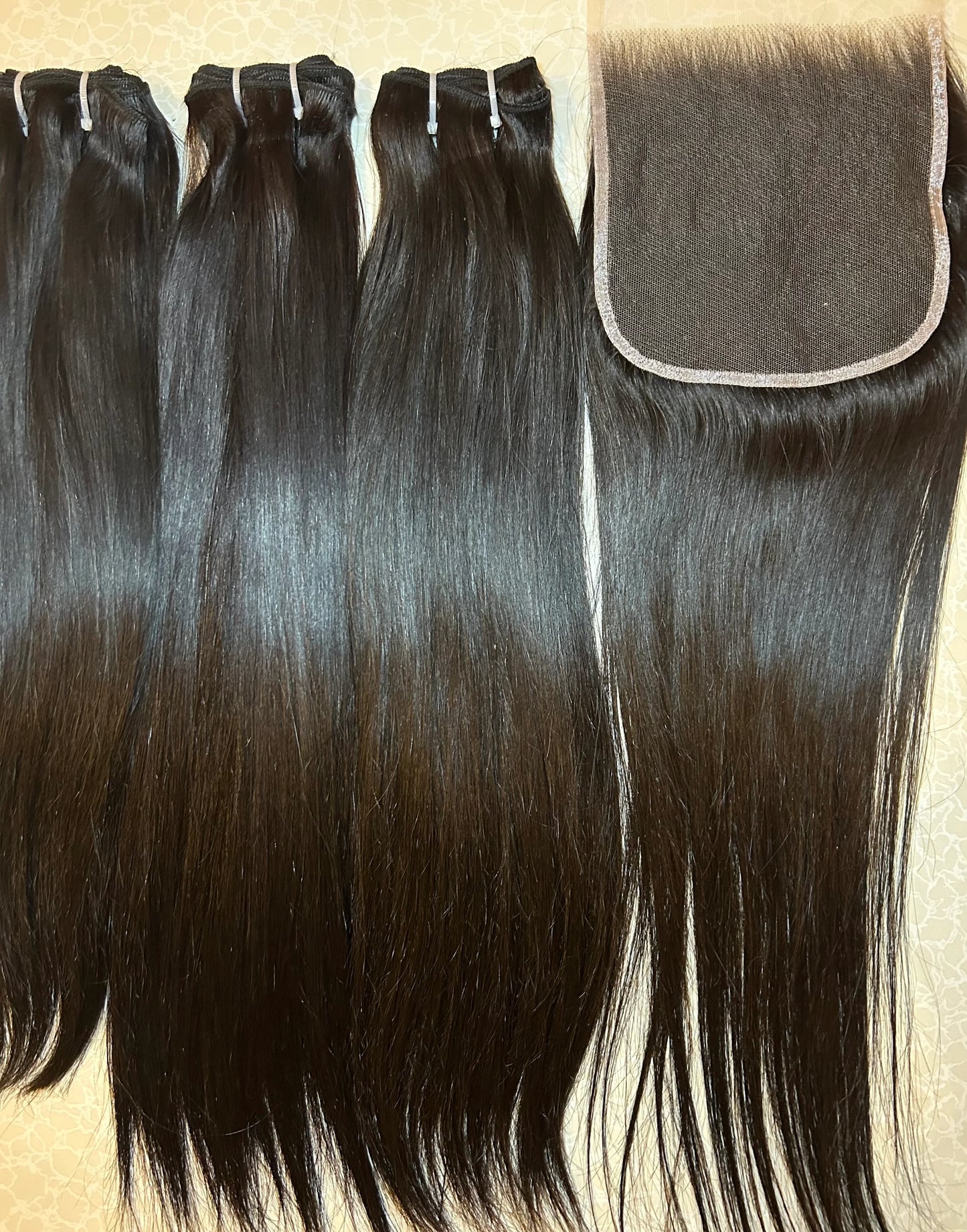 Bundles of straight raw human hair extensions with silk closure on light patterned surface