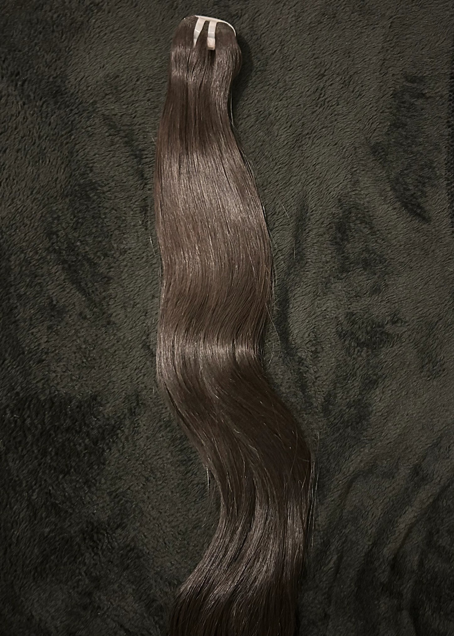 Raw wavy hair extension bundle with natural shine on a dark textured background